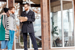 Realtor standing outside, talking a young couple through his checklist on the steps to selling your home.